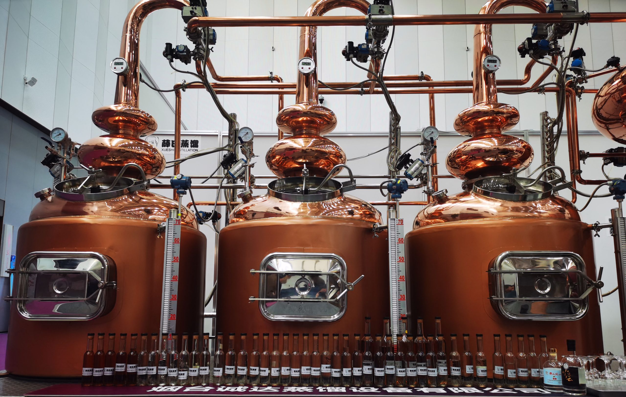 a front view of triple pot still continuous distiller with sample spirits in bottles for exhibition